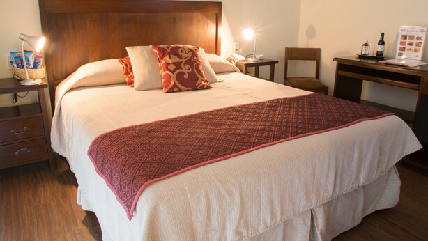 Una cama bien hecha con un edredón estampado, un cabecero de madera y lámparas de noche.