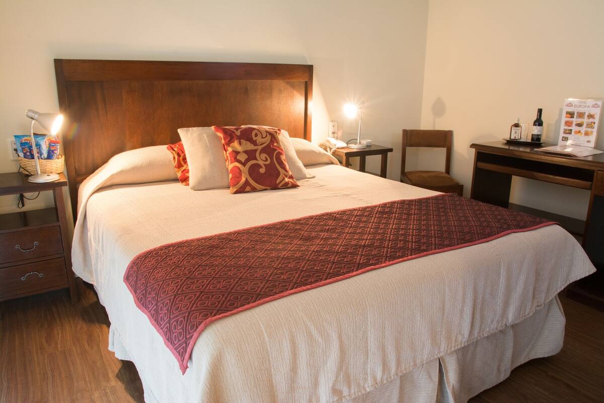 A neatly made bed with a patterned blanket, a wooden headboard, and bedside lamps.