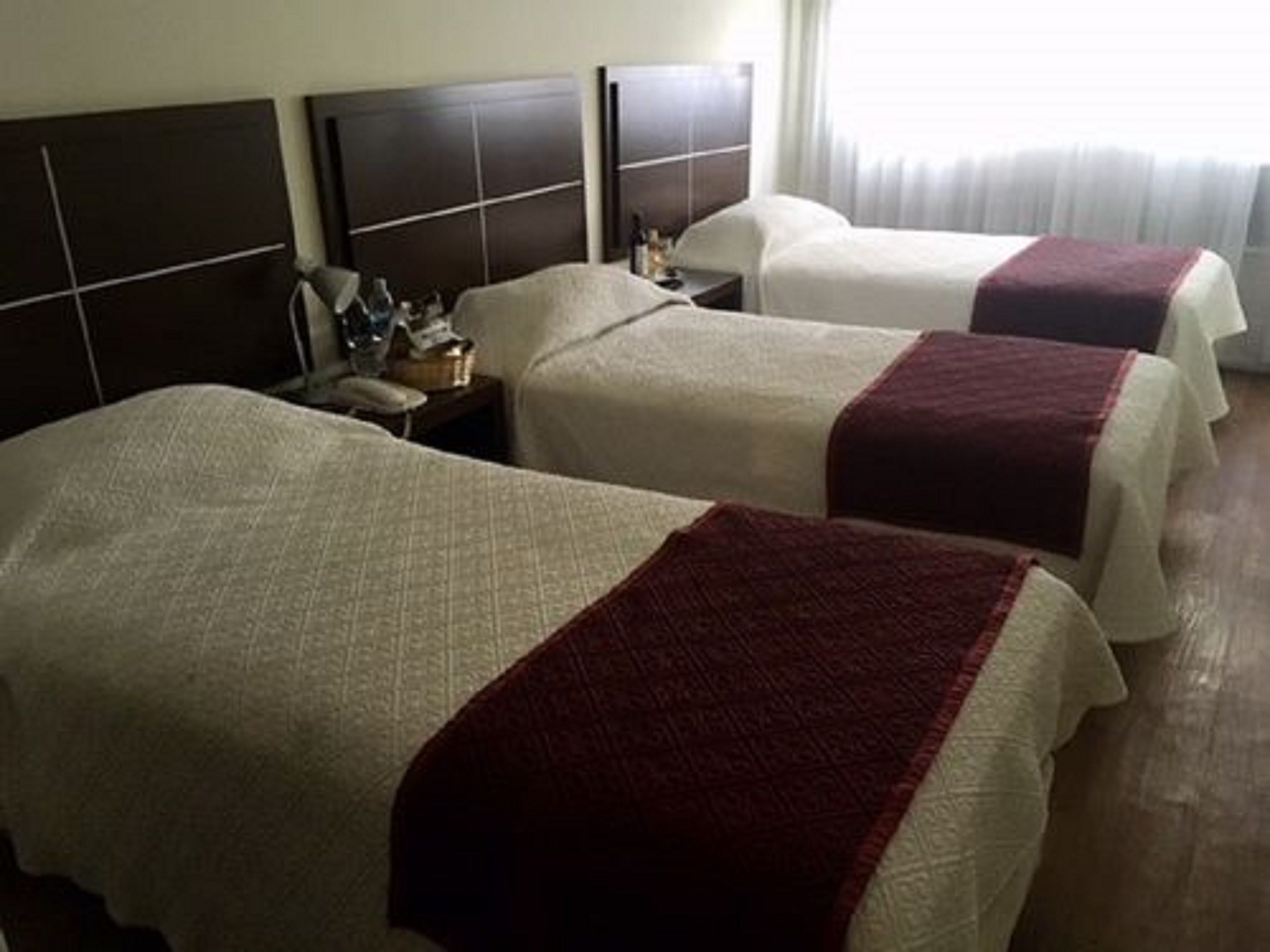 A hotel room with two beds, each with a white bedspread and a red blanket. There is a nightstand with a lamp and a phone between the beds.
