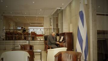 Un hombre tocando el piano en un vestíbulo amplio con una bandera, sillas y un televisor al fondo.