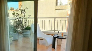 Un balcón con una silla blanca, una mesita con una botella y un vaso, y plantas en macetas.