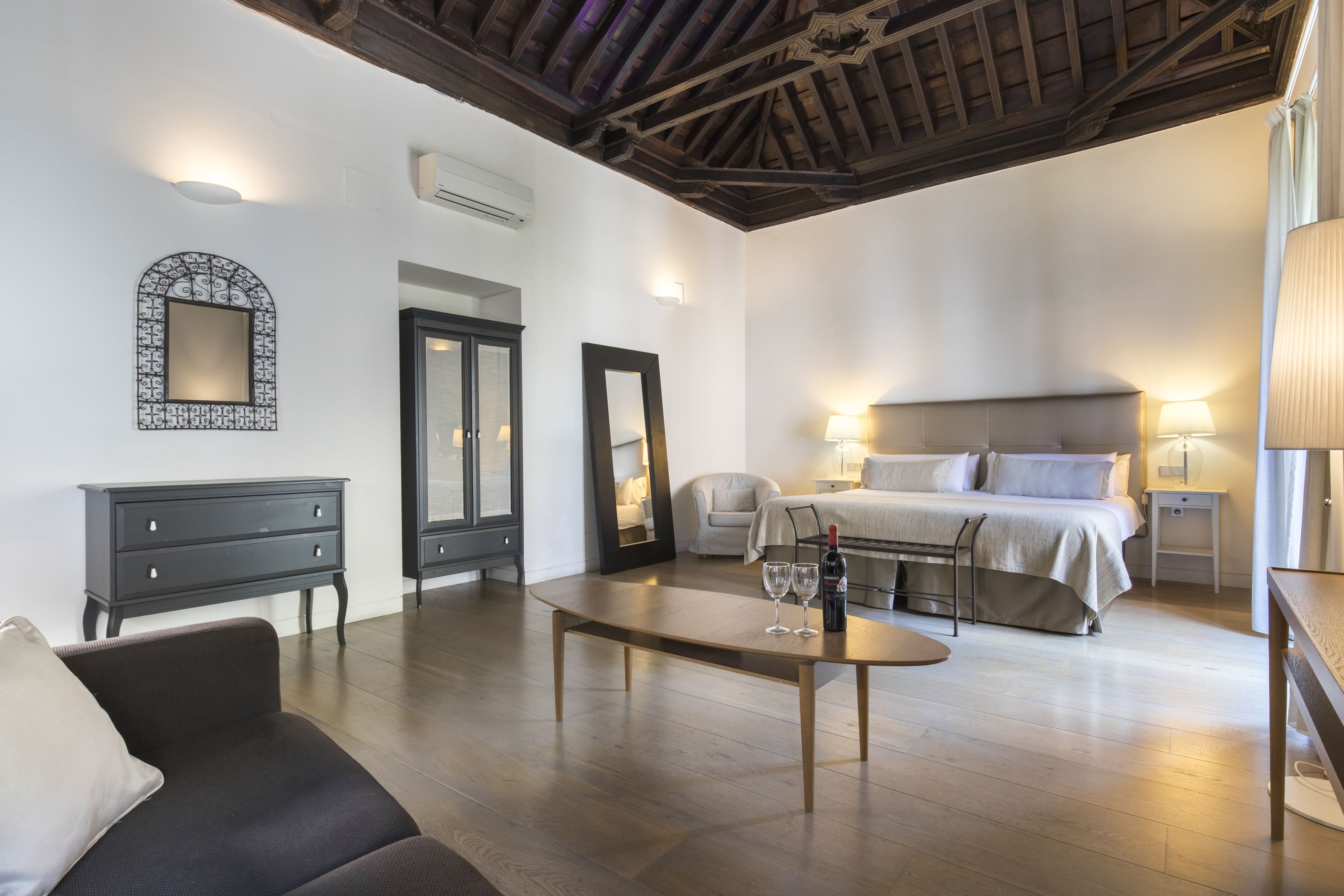 Una habitación de hotel moderna con una cama, mesitas de noche, un sofá, una mesa de centro y un espejo.