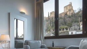 A hotel room with a large bed, two armchairs, a small table, and a view of a historic building through large windows. - Shine Albayzín Hotel (Granada)
