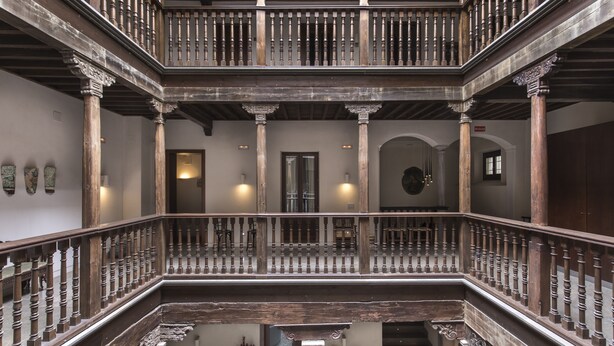 A multi-level wooden staircase with ornate balustrades and columns, leading to a balcony. - Shine Albayzín Hotel (Granada)