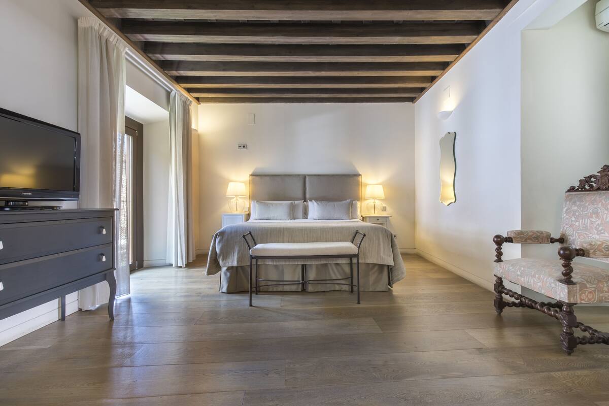 Un dormitorio con cama, lámparas de noche, un banco, cómoda y televisor.