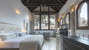 A bedroom with a large bed, a TV, and a view of buildings through the window. - Shine Albayzín Hotel (Granada)
