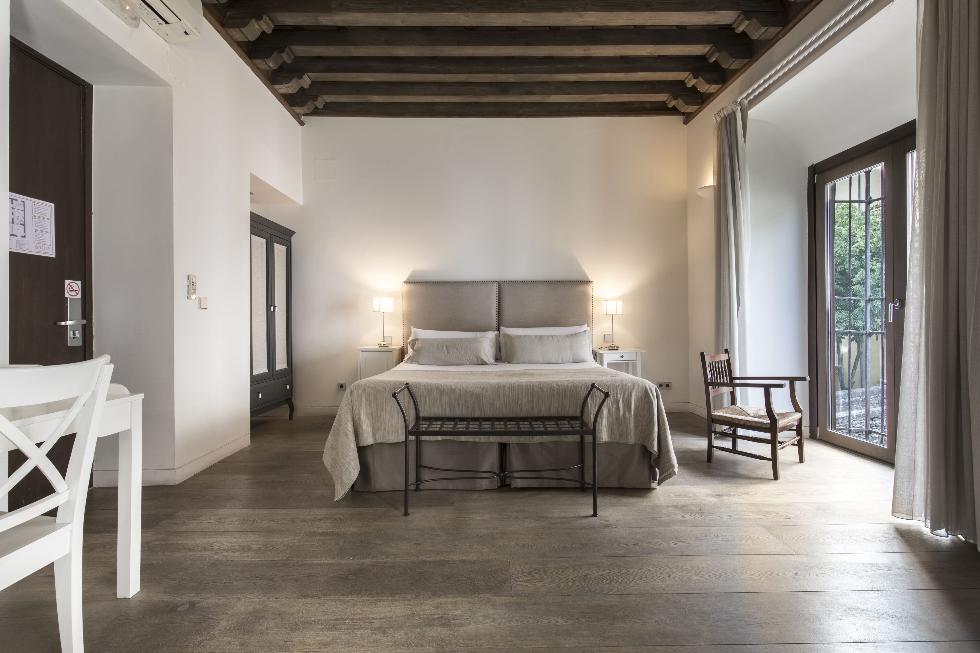 Un dormitorio con cama, mesitas de noche, un banco y una silla.