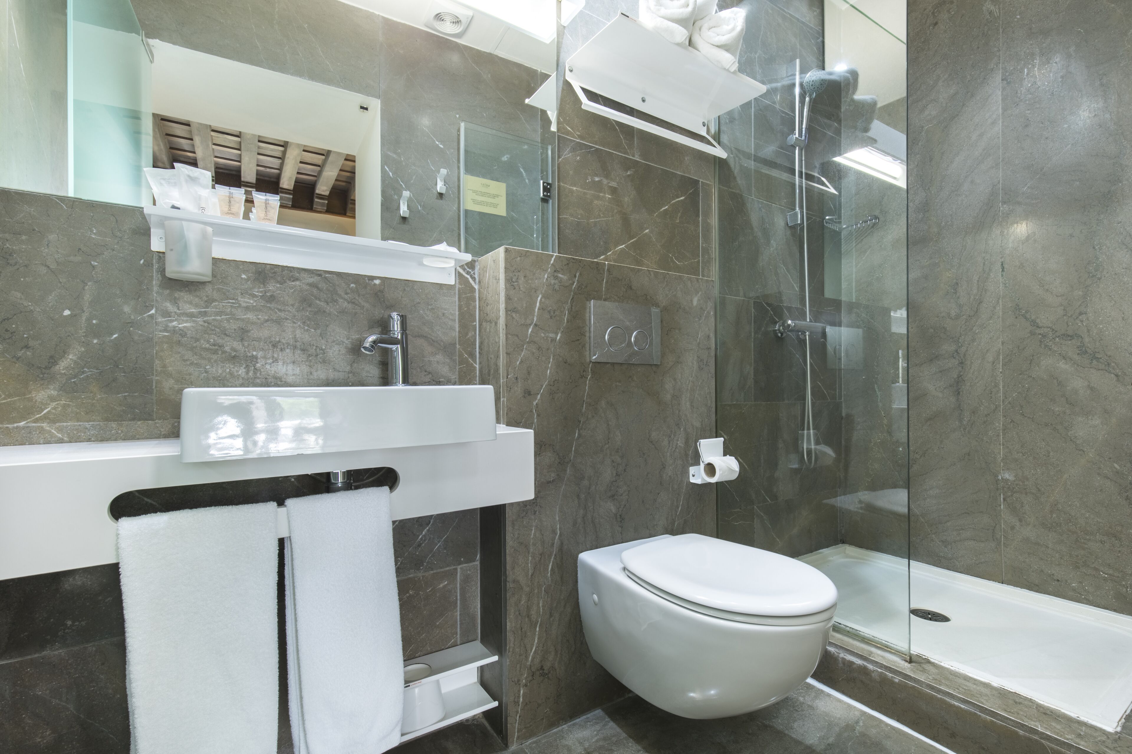 Un baño moderno con cabina de ducha de vidrio, inodoro blanco y pared revestida de mármol.