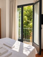 Una habitación con cama, un balcón con barandilla de metal y vistas al verdor exterior.
