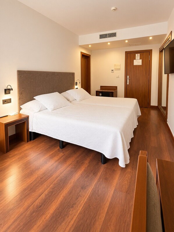 A hotel room with a large bed, bedside tables, a wooden floor, and a television on the wall. - Monjas Del Carmen Hotel (Granada)