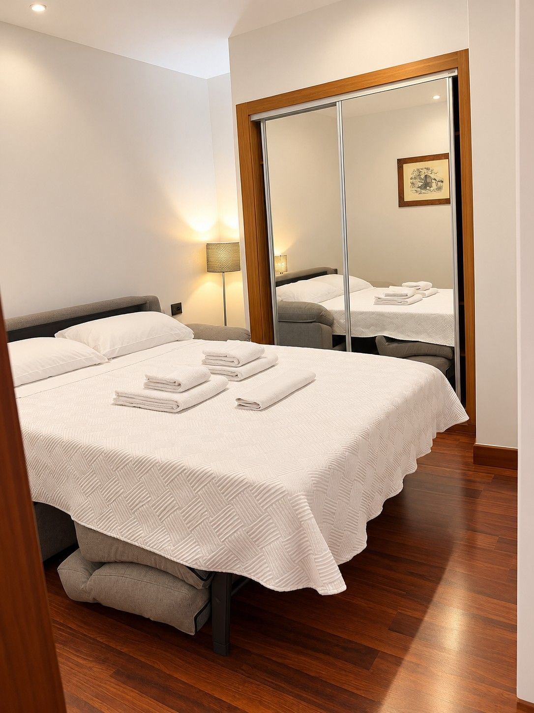 Una habitación de hotel con una cama grande, un espejo y una lámpara de noche.