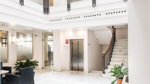 En moderne hotellobby med en trappe i marmor, en receptionsdisk og en glas elevator.