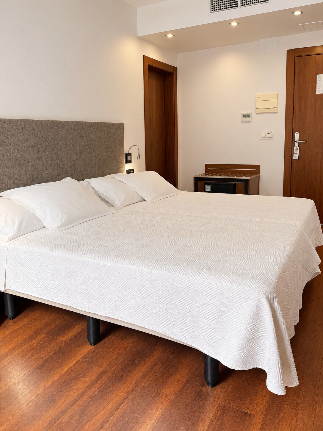 Een hotelkamer met een groot bed, een houten hoofdeinde, een nachtkastje en een deur.