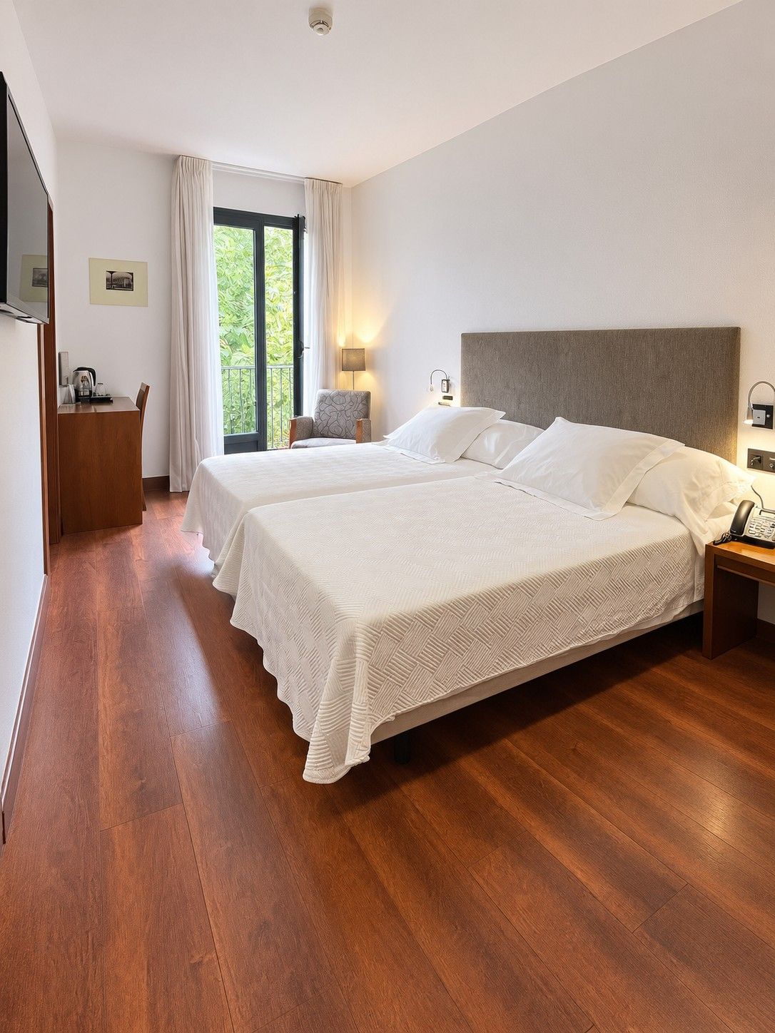 Una camera d'albergo con un letto matrimoniale, una scrivania, una sedia, una televisione e una finestra con tende.