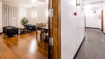 A hotel room with a wooden door, a dining area with a table and chairs, and a carpeted hallway.