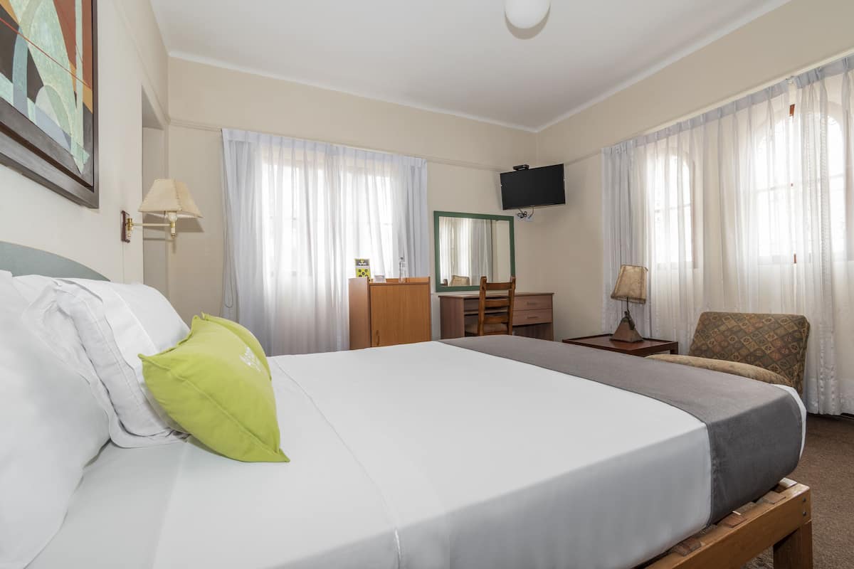 A hotel room with a bed, a desk, a chair, a TV, and a window with curtains.