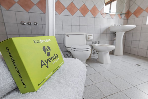 A bathroom with a white toilet, bidet, and sink. A green box labeled "Ayenda Hotels" is on a white fluffy rug. - San Isidro Inn (Lima)