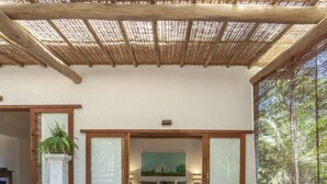 A spacious room with a wooden floor, a white sofa with blue cushions, and a large window with a view of trees. - Etnia Casa Hotel (Porto Seguro)