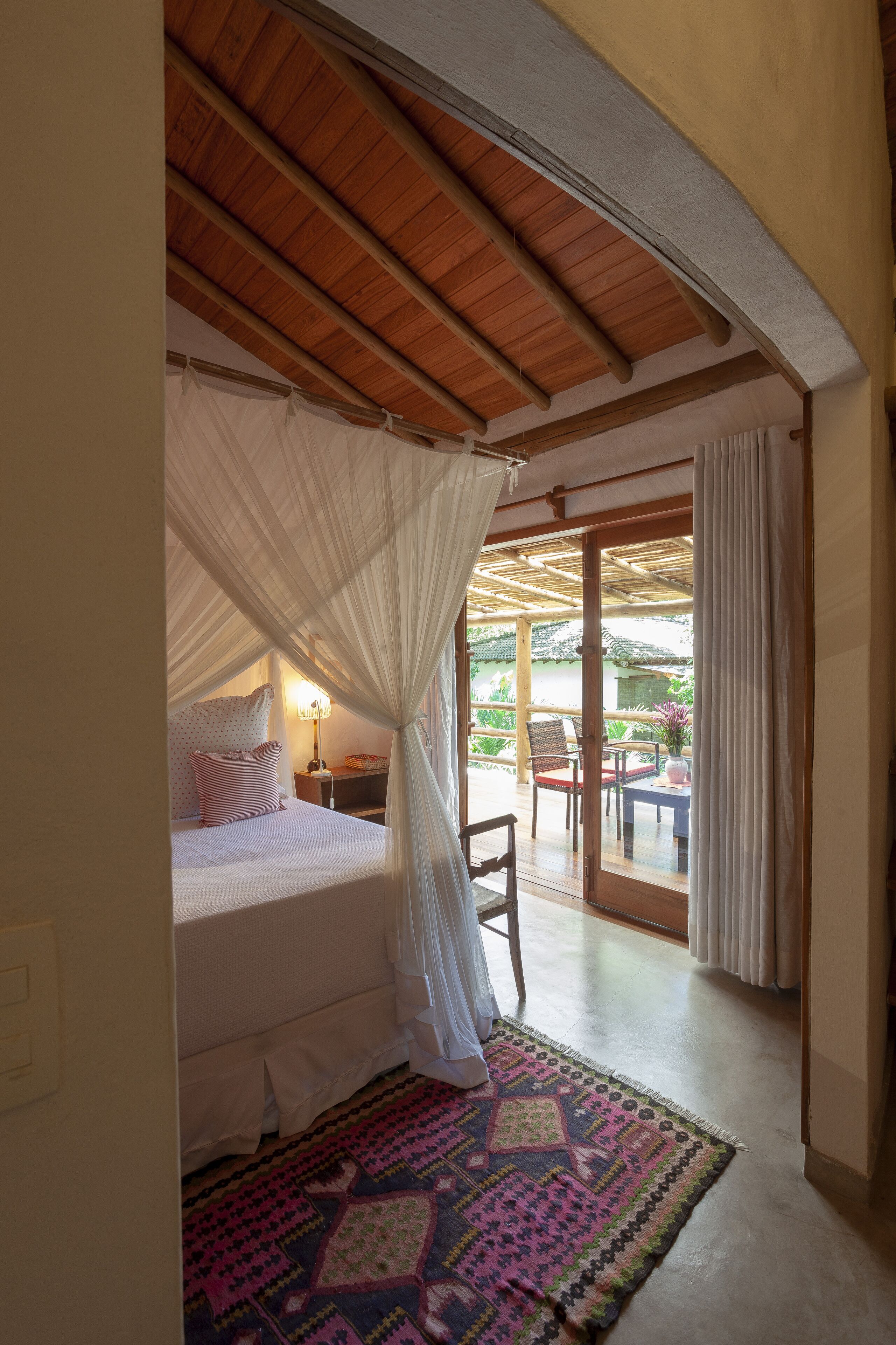 A bedroom with a canopy bed, a patterned rug, and a view of the outdoor patio area.