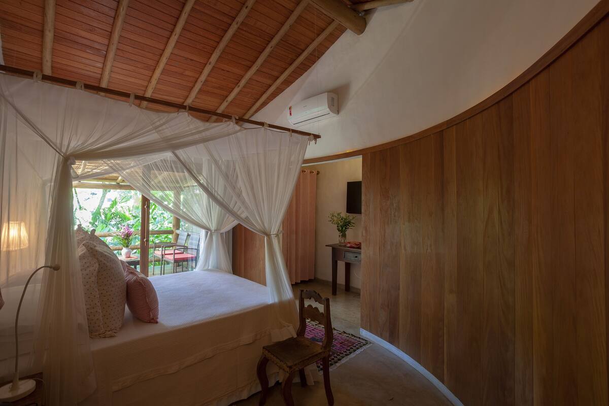 Een slaapkamer met een hemelbed, houten wanden, een tafeltje met een vaas en een stoel.