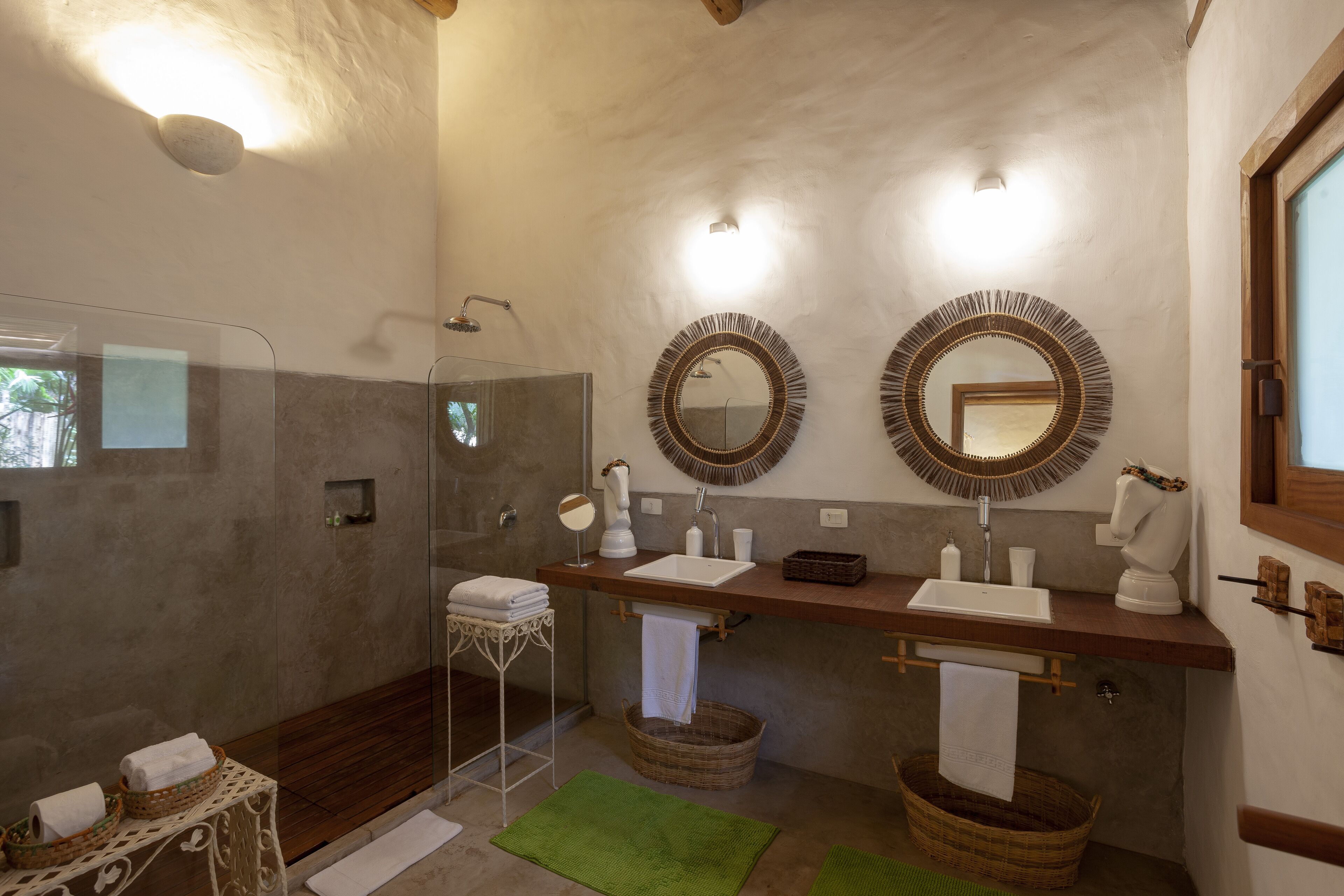 A bathroom with a glass shower enclosure, two sinks with round mirrors, and wicker baskets.