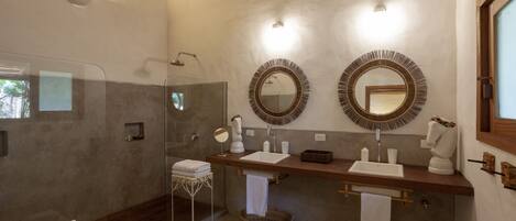 A bathroom with a glass shower enclosure, two sinks with round mirrors, and wicker baskets.