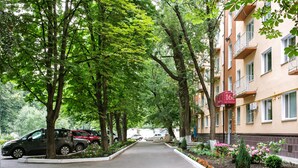 Une rue bordée d’arbres, avec des voitures garées et un immeuble doté de balcons.