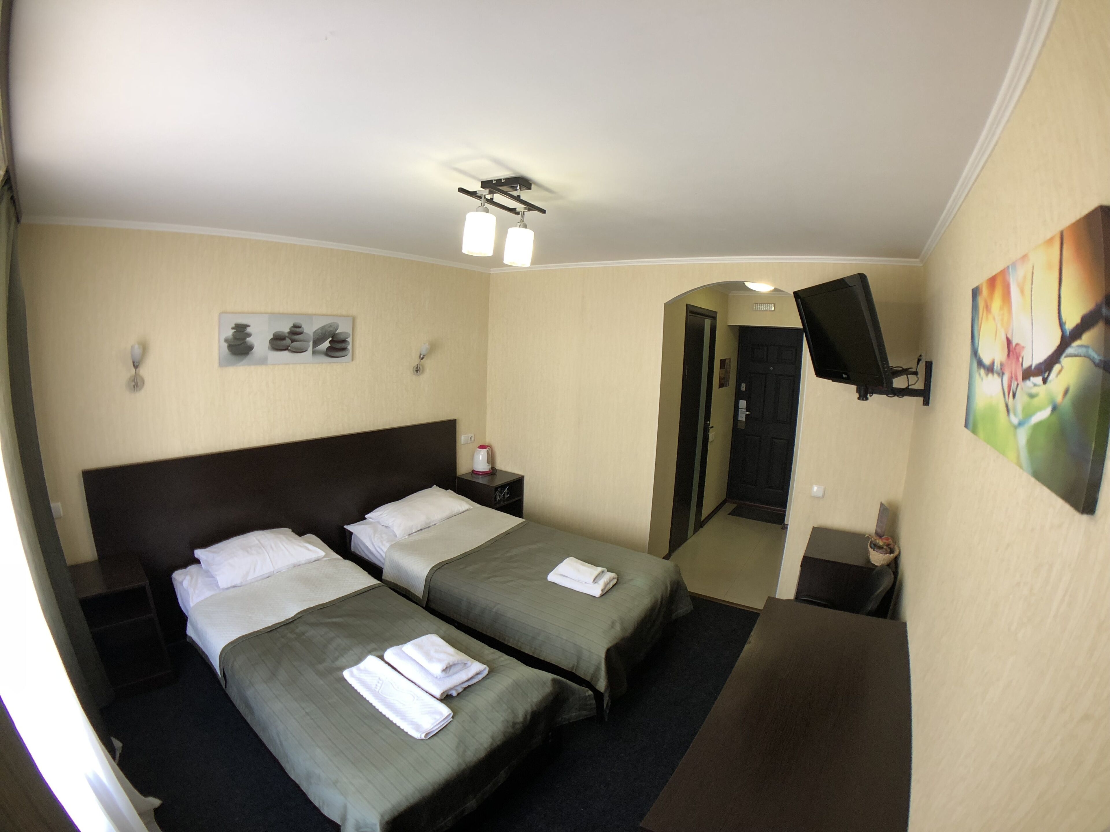 A hotel room with two beds, a flat-screen TV mounted on the wall, a painting, and a small table with a kettle.
