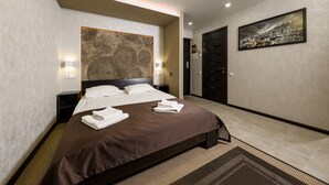 Une chambre d’hôtel moderne avec un grand lit, une tête de lit agrémentée d’un décor mural texturé, un tableau au mur et une porte sombre.