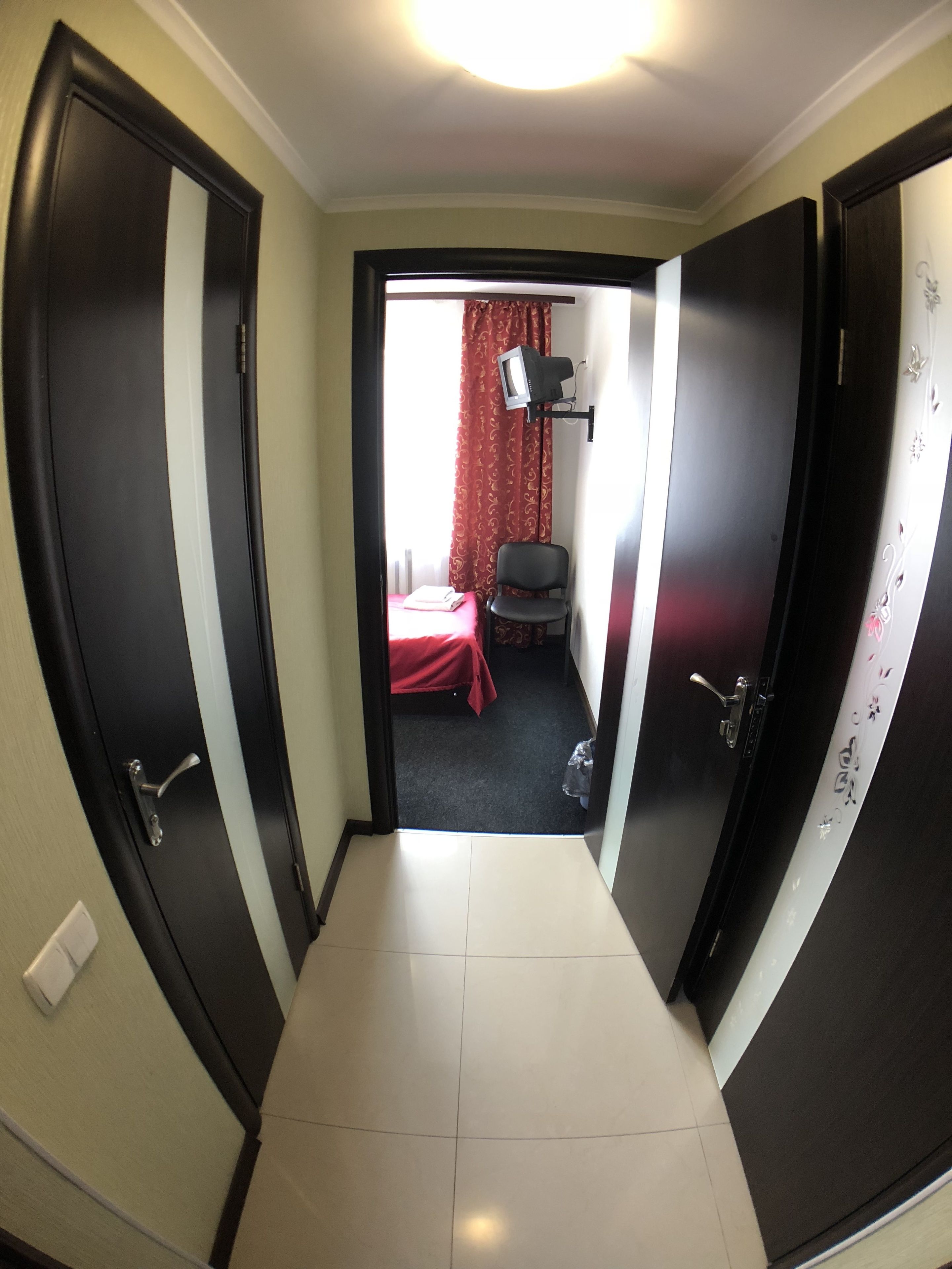 A corridor leading to a room with a bed, a chair, and a television on a stand.