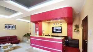 Un espace d’accueil aux couleurs rouge et beige, doté d’un téléviseur à écran plat, d’une horloge et d’une plante en pot.
