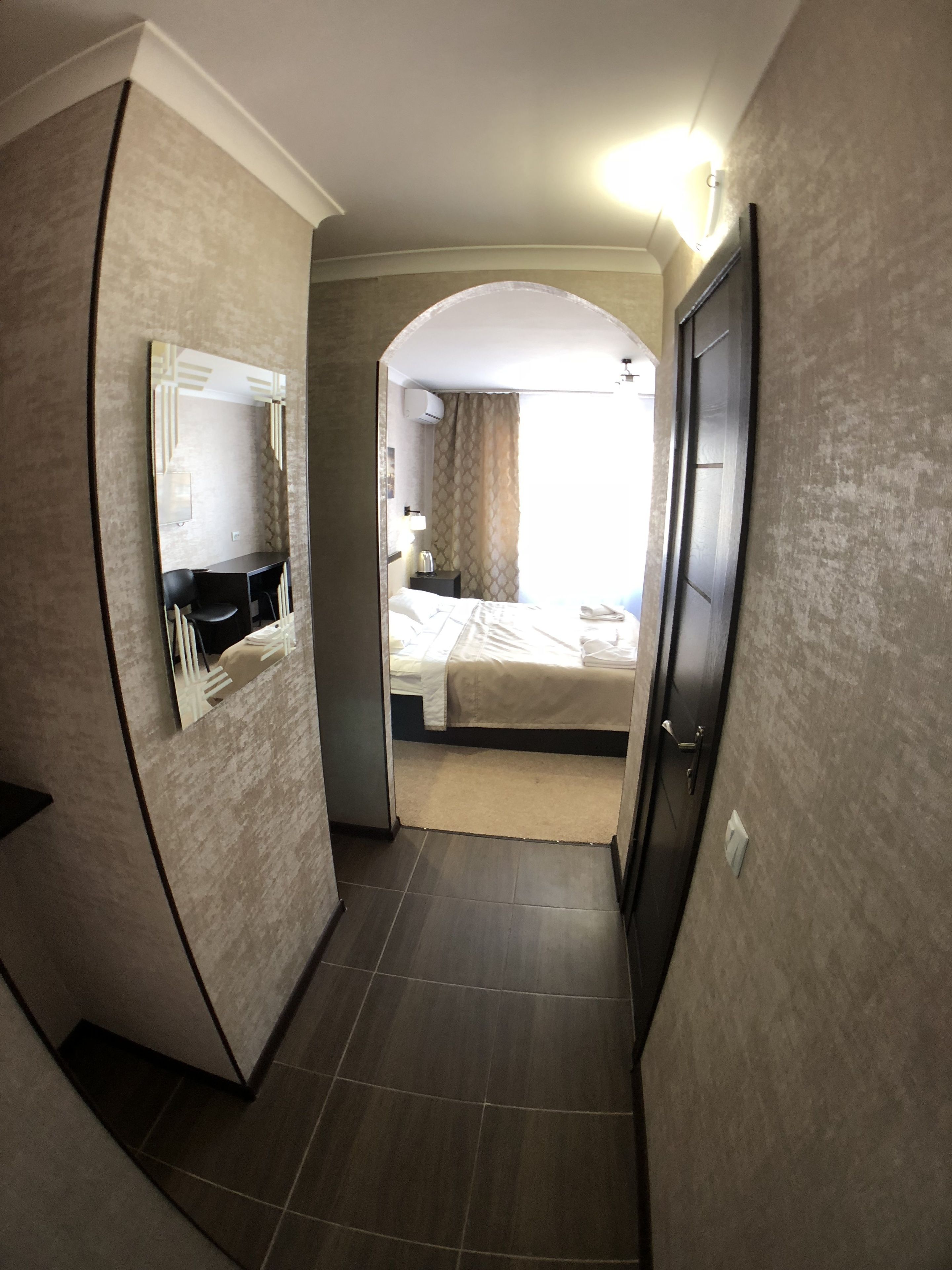A narrow hallway leading to a bedroom with a bed, a nightstand, and a mirror.