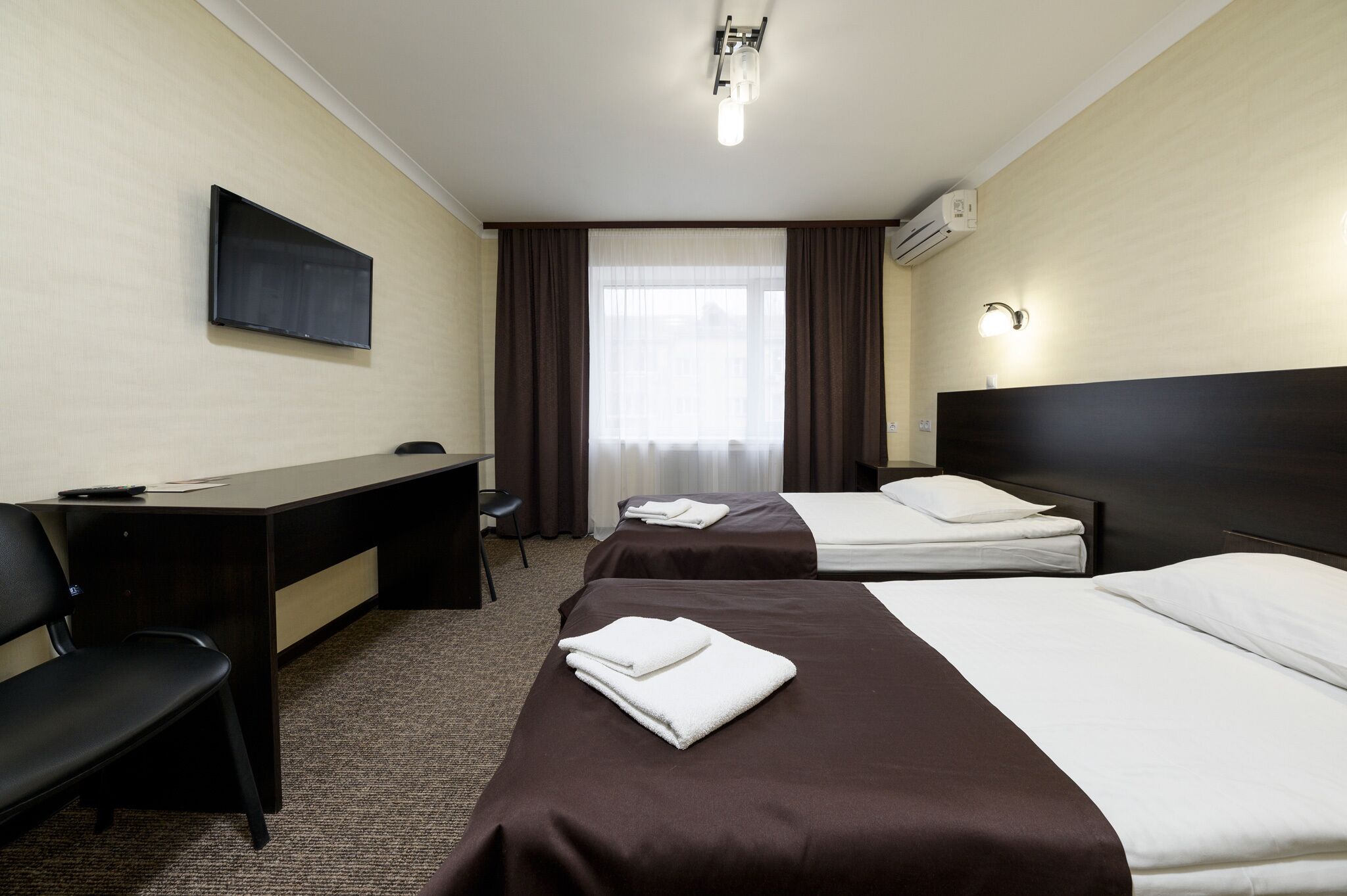Habitación de hotel con dos camas, un escritorio, una silla, un televisor y una ventana con cortinas.