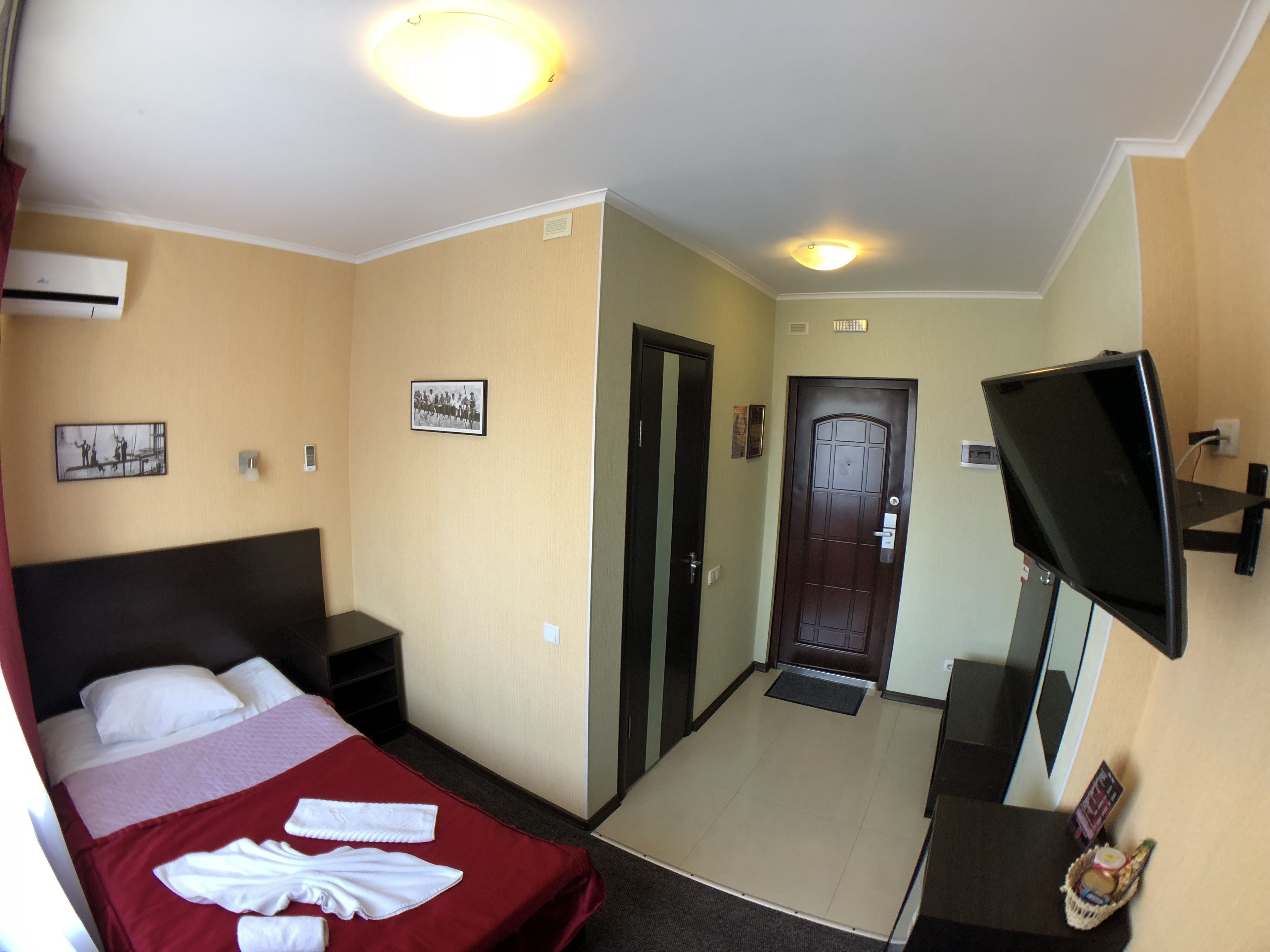 A hotel room with a bed, a television, a door, and a wall-mounted air conditioning unit.