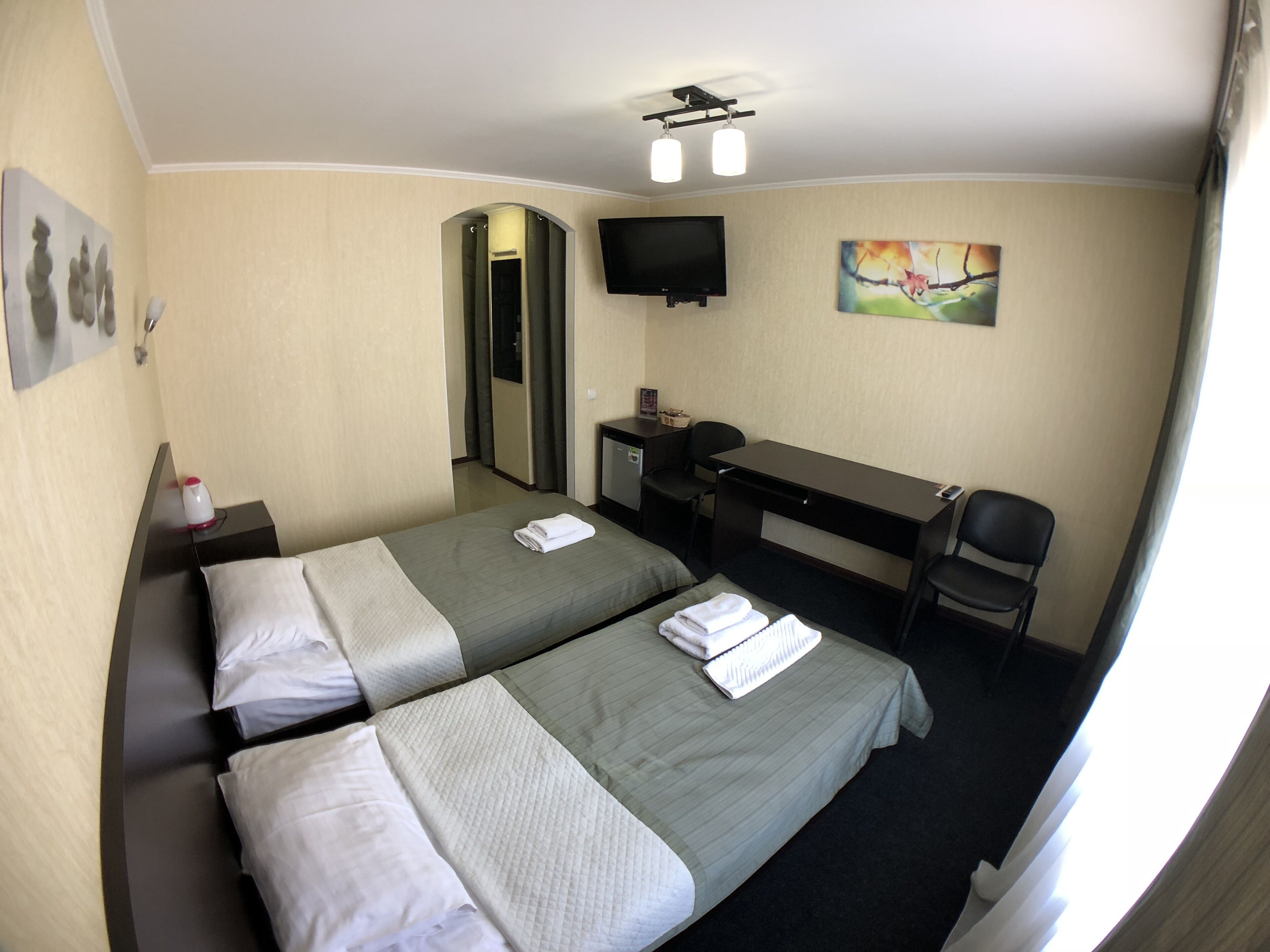 Een hotelkamer met twee bedden, een bureau, een stoel, een televisie en een schilderij aan de muur.