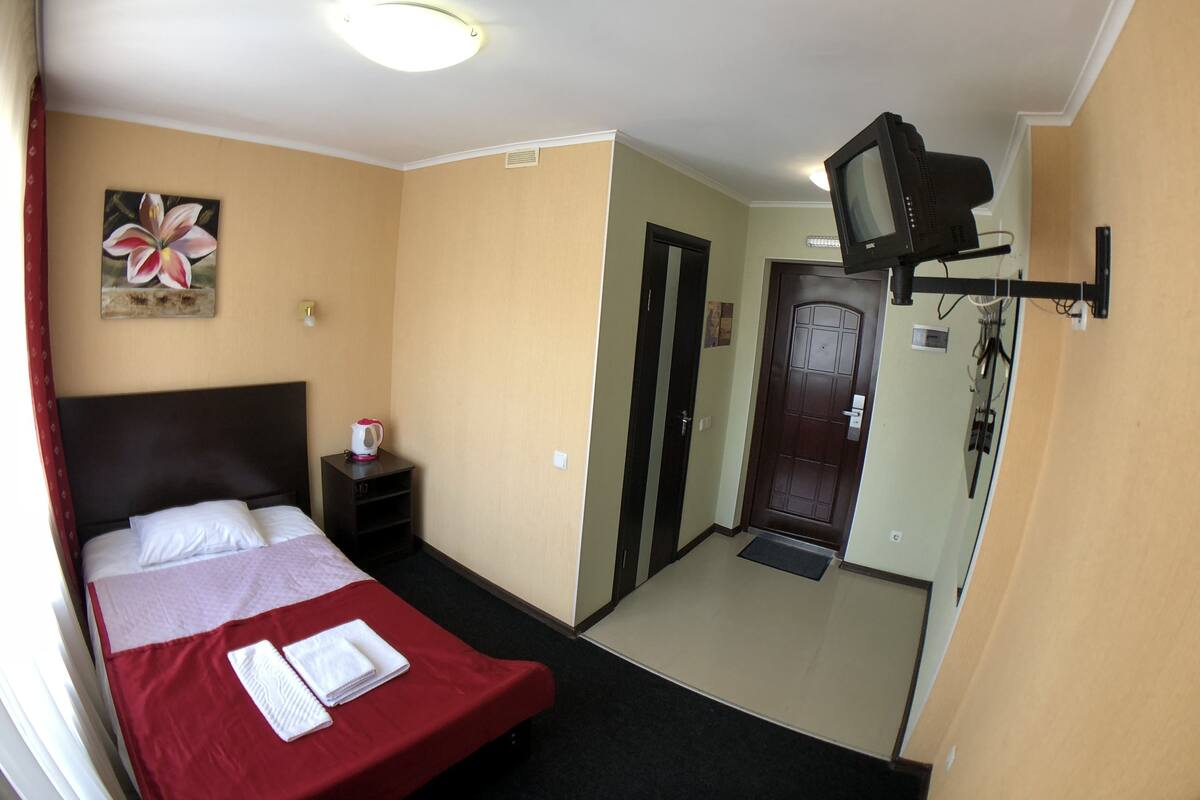 A hotel room with a bed, a television mounted on the wall, a door, and a small table with a kettle.