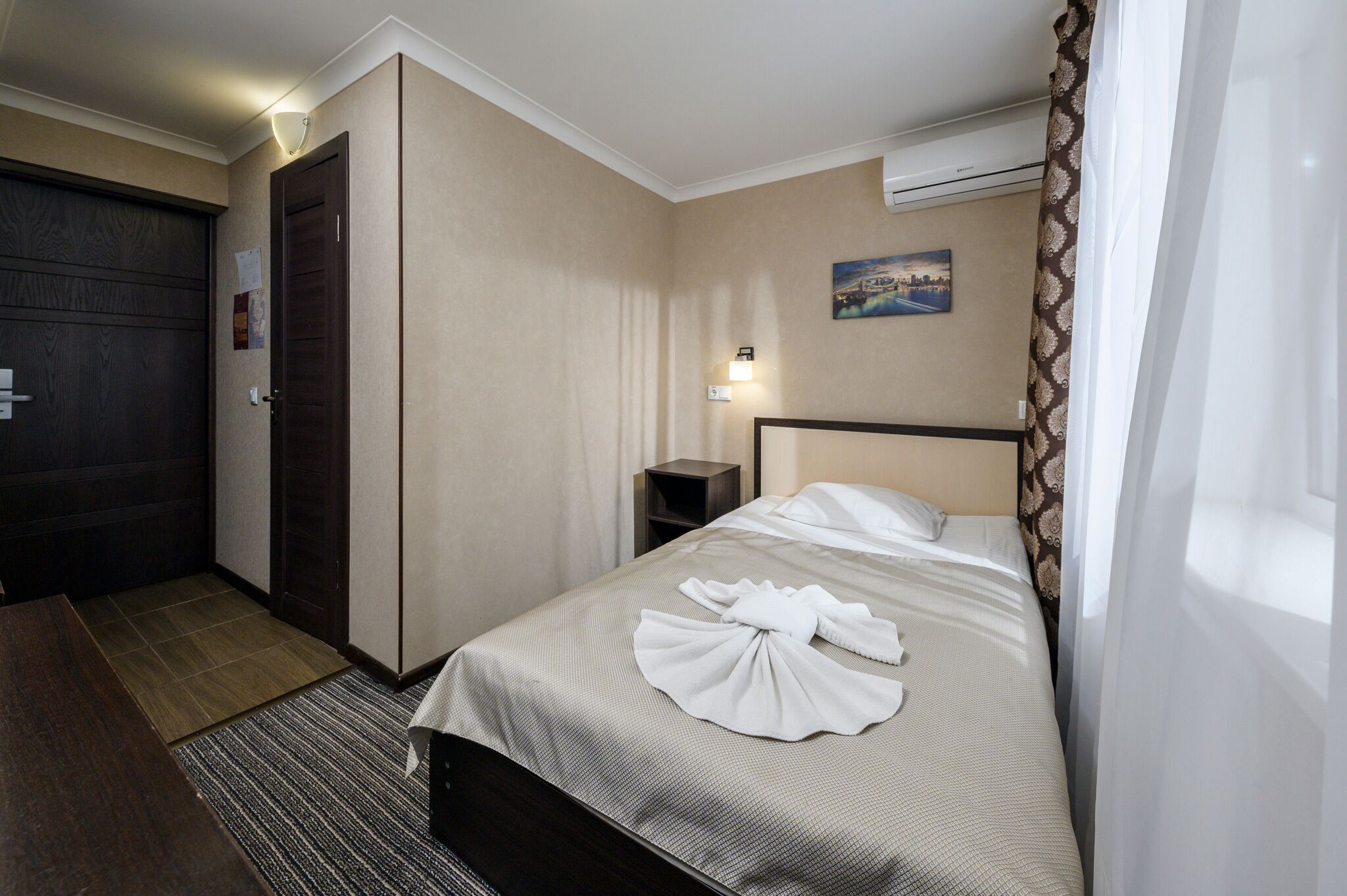 A hotel room with a bed, a nightstand, a wall-mounted air conditioner, and a door.