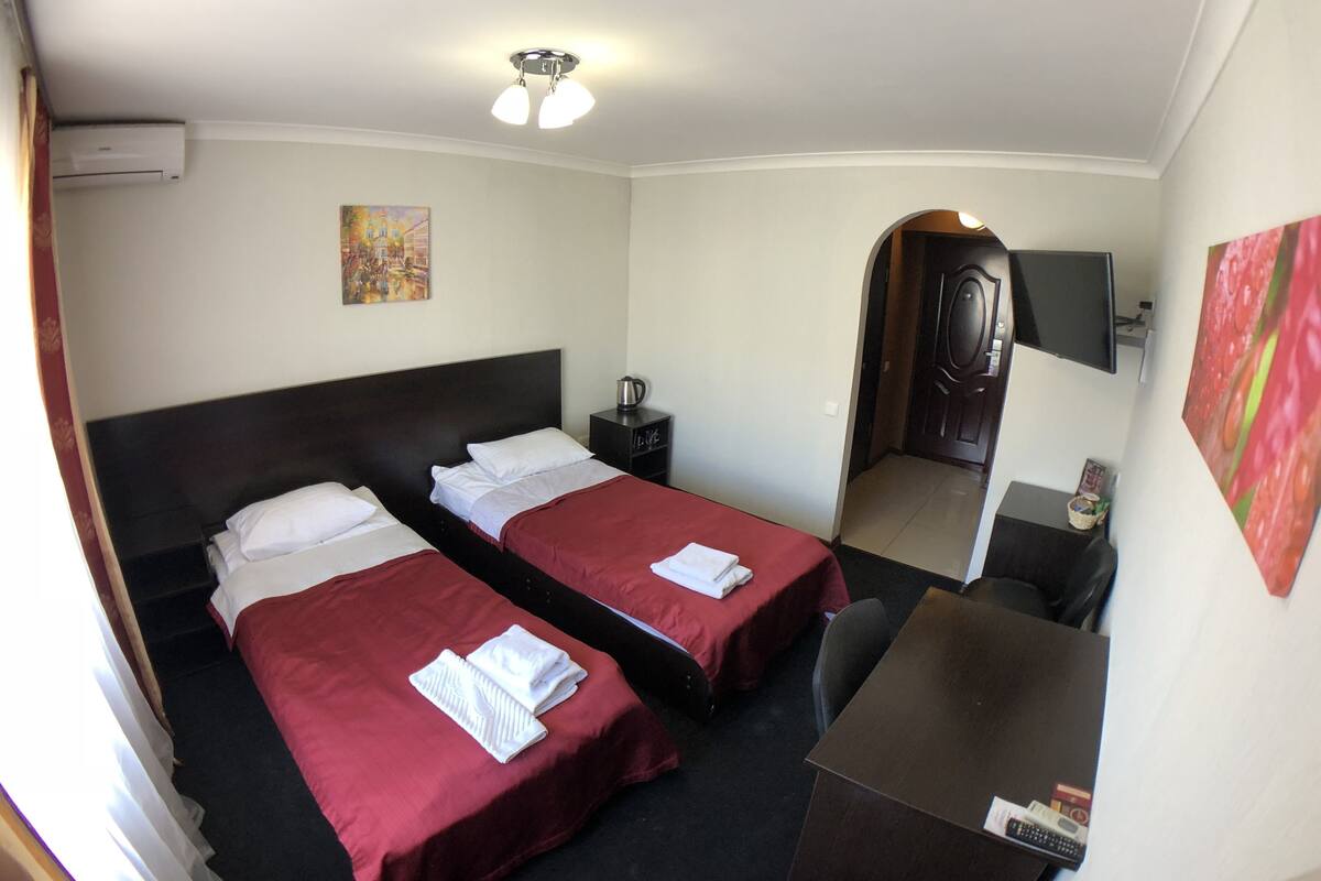 A hotel room with two beds, a desk, a chair, a TV, and a painting on the wall.