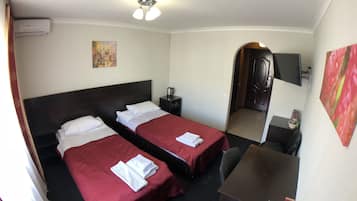 A hotel room with two beds, a desk, a chair, a TV, and a painting on the wall.