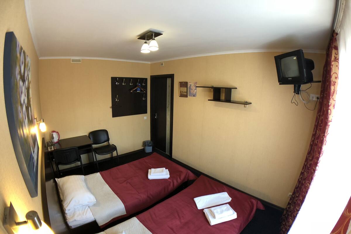 A hotel room with two beds, a desk, a chair, a TV, and a painting on the wall.