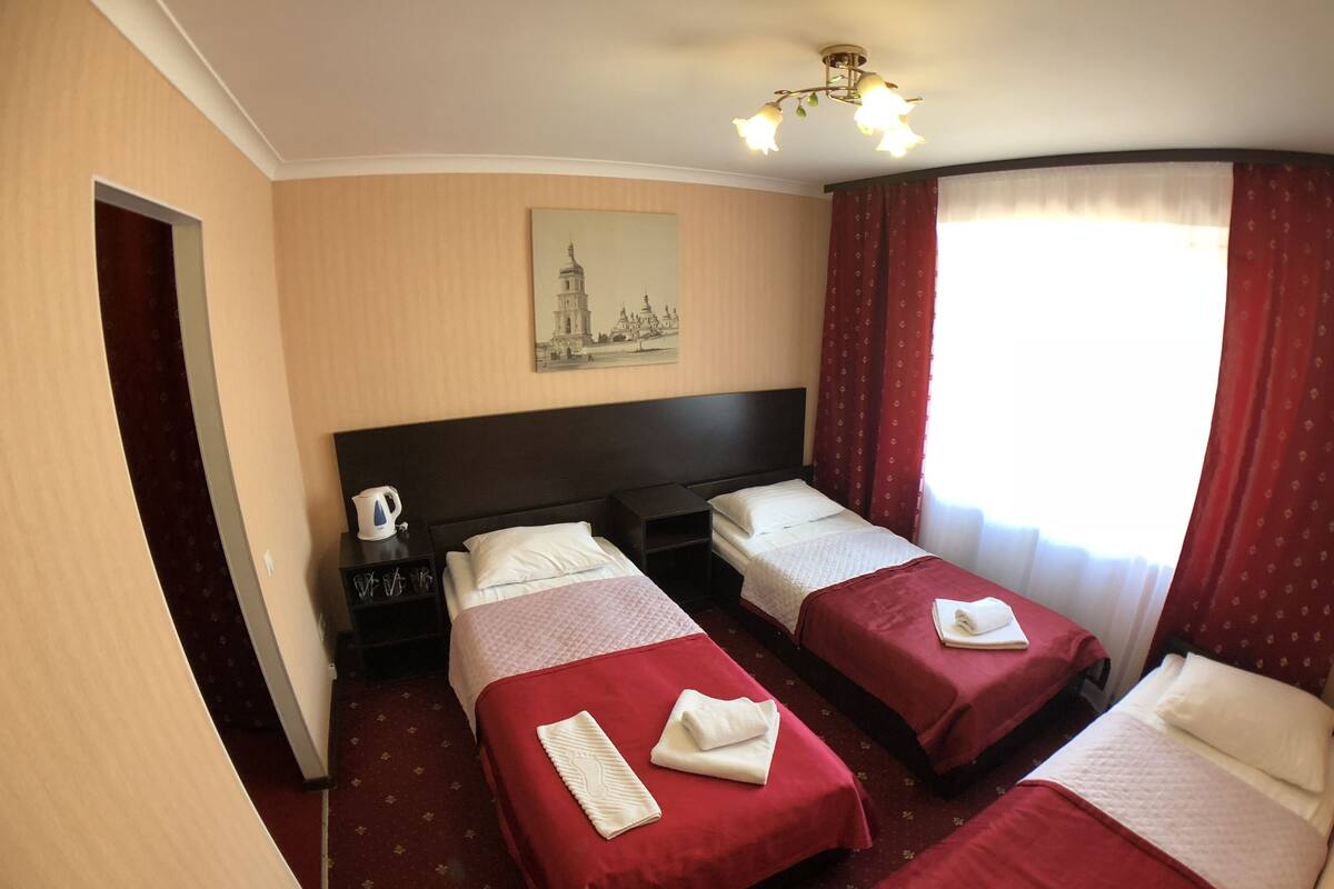 A hotel room with two beds, a painting of a cityscape, a coffee maker, and a window with curtains.