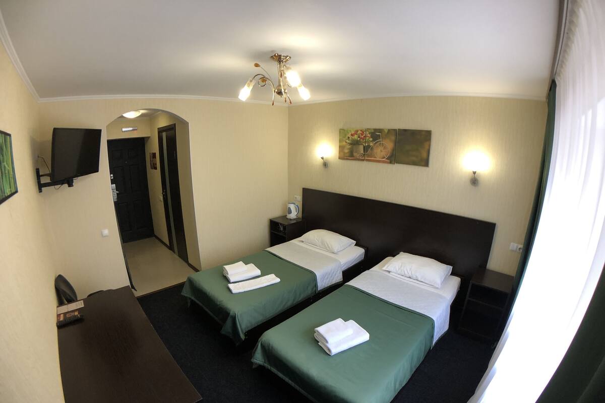 A hotel room with two single beds, a desk, a chair, a television, and a painting on the wall.
