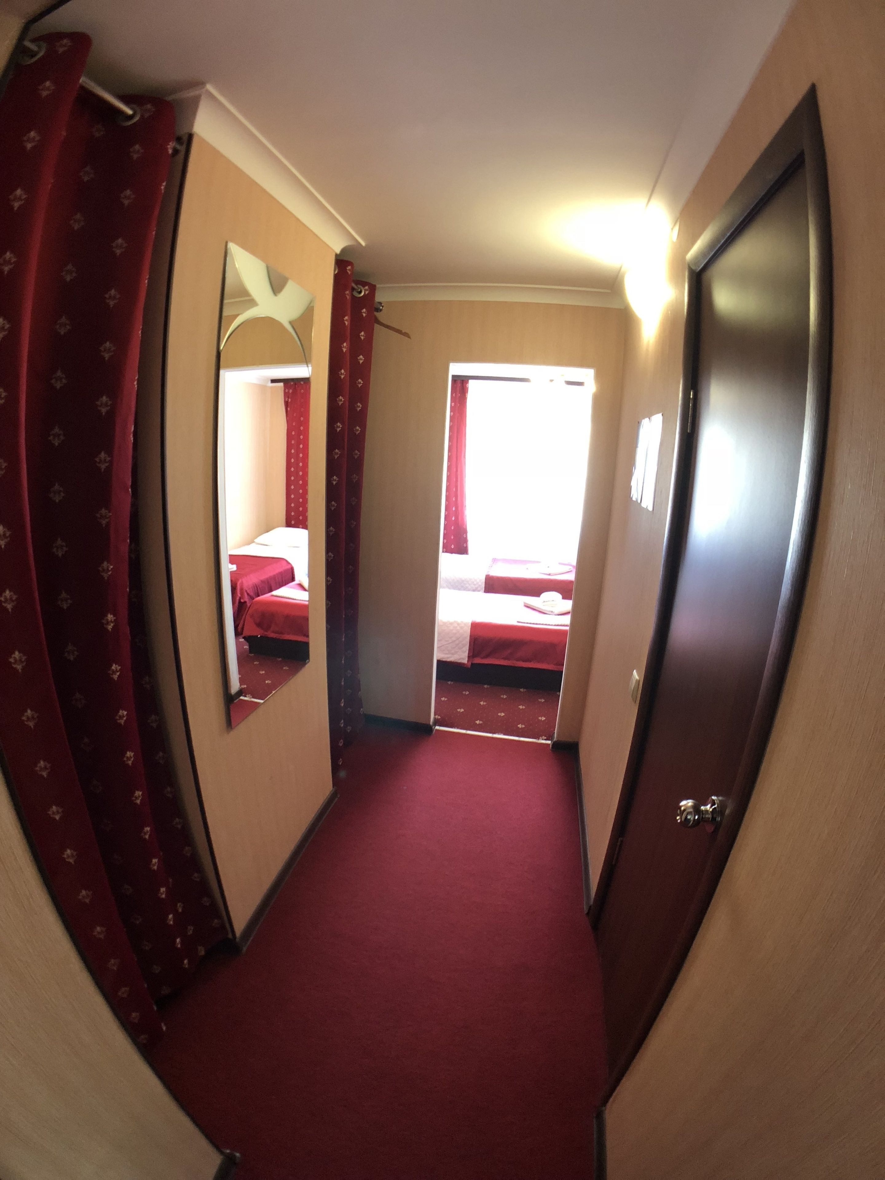 Um corredor estreito com carpete vermelho que leva a um quarto com cama e janela.