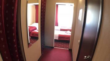 Um corredor estreito com carpete vermelho que leva a um quarto com cama e janela.