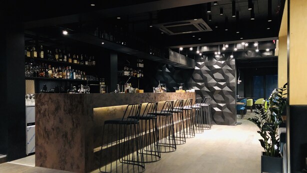 Un espace bar avec un comptoir, de nombreux tabourets et des étagères remplies de bouteilles.