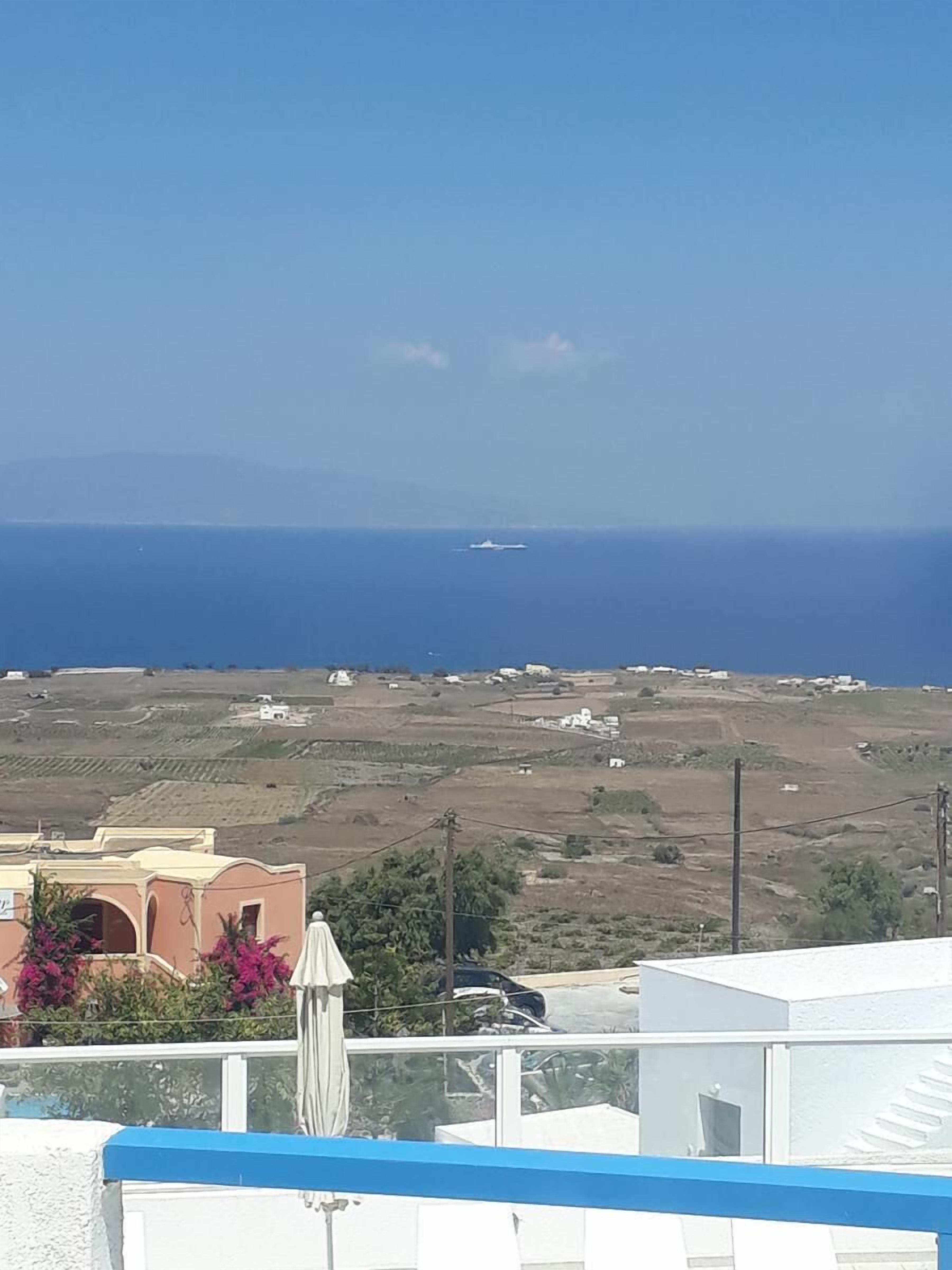 A coastal view with a clear sky, a distant ship, and a landscape with scattered buildings.