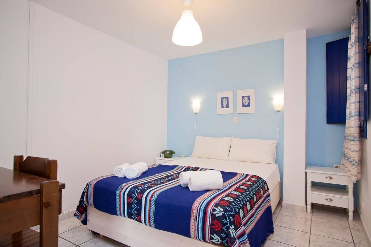 A bedroom with a bed, a bedside table, a nightstand, a chair, and a wall-mounted telephone.