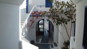 Un estrecho pasaje con pared blanca y detalles azules, que conduce a una escalera y una puerta.