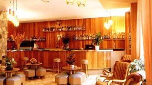 Een bar met houten lambrisering, meerdere barkrukken en diverse flessen op planken.