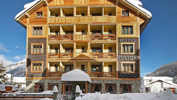Een meerlaags hotel met balkons, een gevel van natuursteen en een bord dat aangeeft dat het een vakantiehotel is.